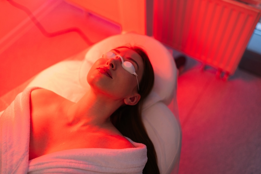 Patient undergoing photodynamic therapy (PDT) treatment under red light, wearing protective goggles in a clinical setting.