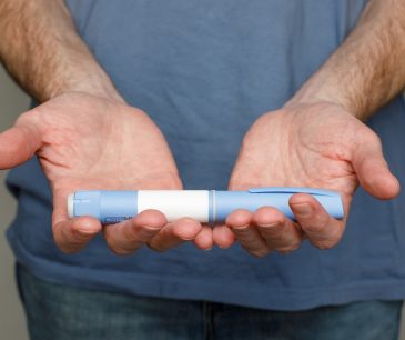 Close-up of man holding Ozempic injection pen in both hands, illustrating weight loss treatment and its facial side effects